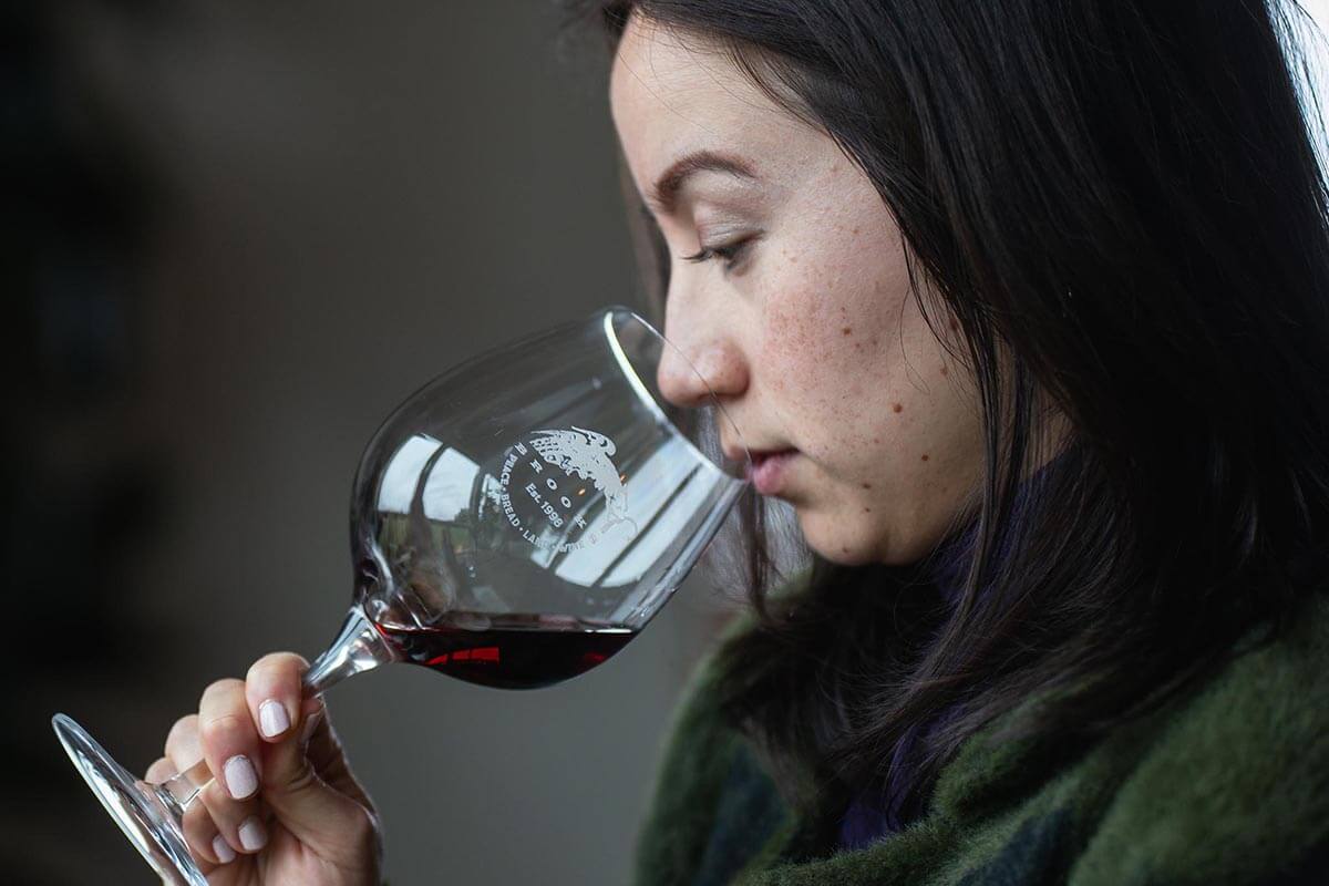 A young Asian woman with dark hair intently smells a glass of Pinot Noir as she studies the wine's qualities and potential faults.