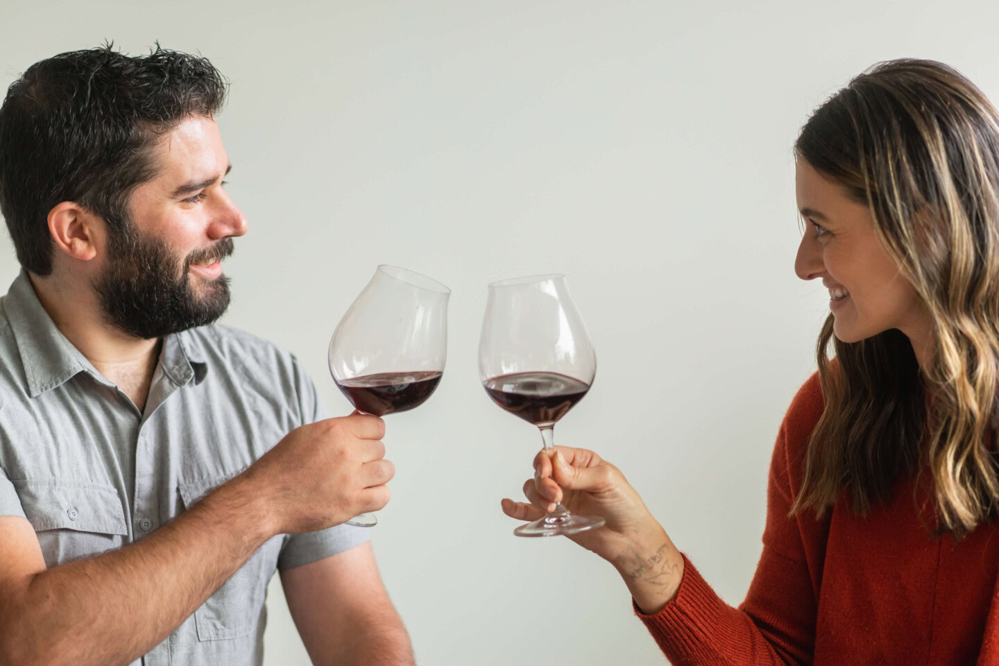 A man in a short sleeved Polo shirt and woman in a red sweater toast wine glasses of Pinot Noir while enjoying a tasting in Portland, Oregon. 